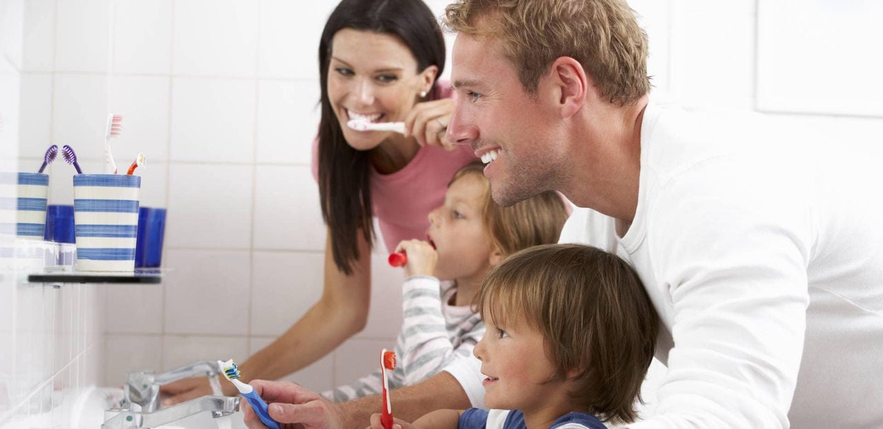 Padres e hijos sonrientes lavándose los dientes juntos frente al espejo del baño